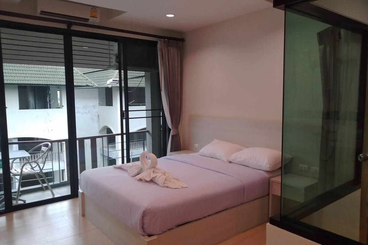 A bedroom with a bed, a glass door, and a balcony with a chair.