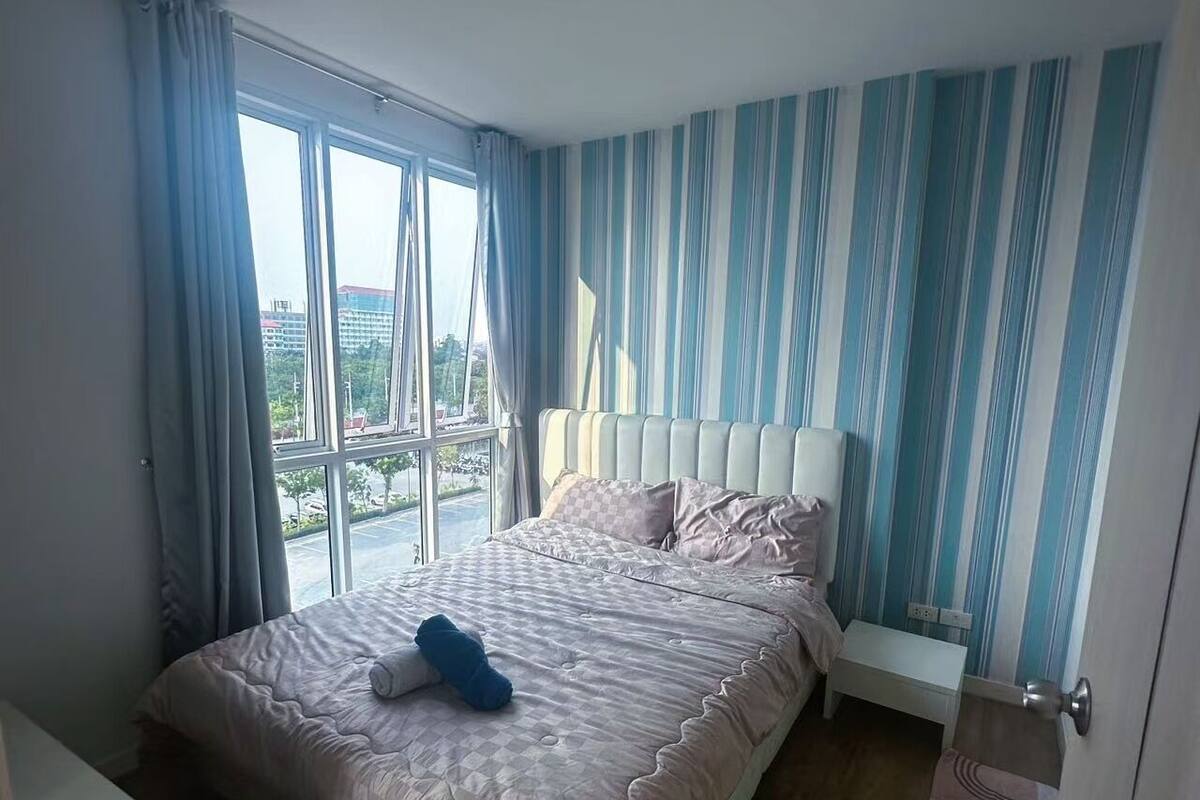 A bedroom with a large bed, a bedside table, a window with curtains, and a striped wall.
