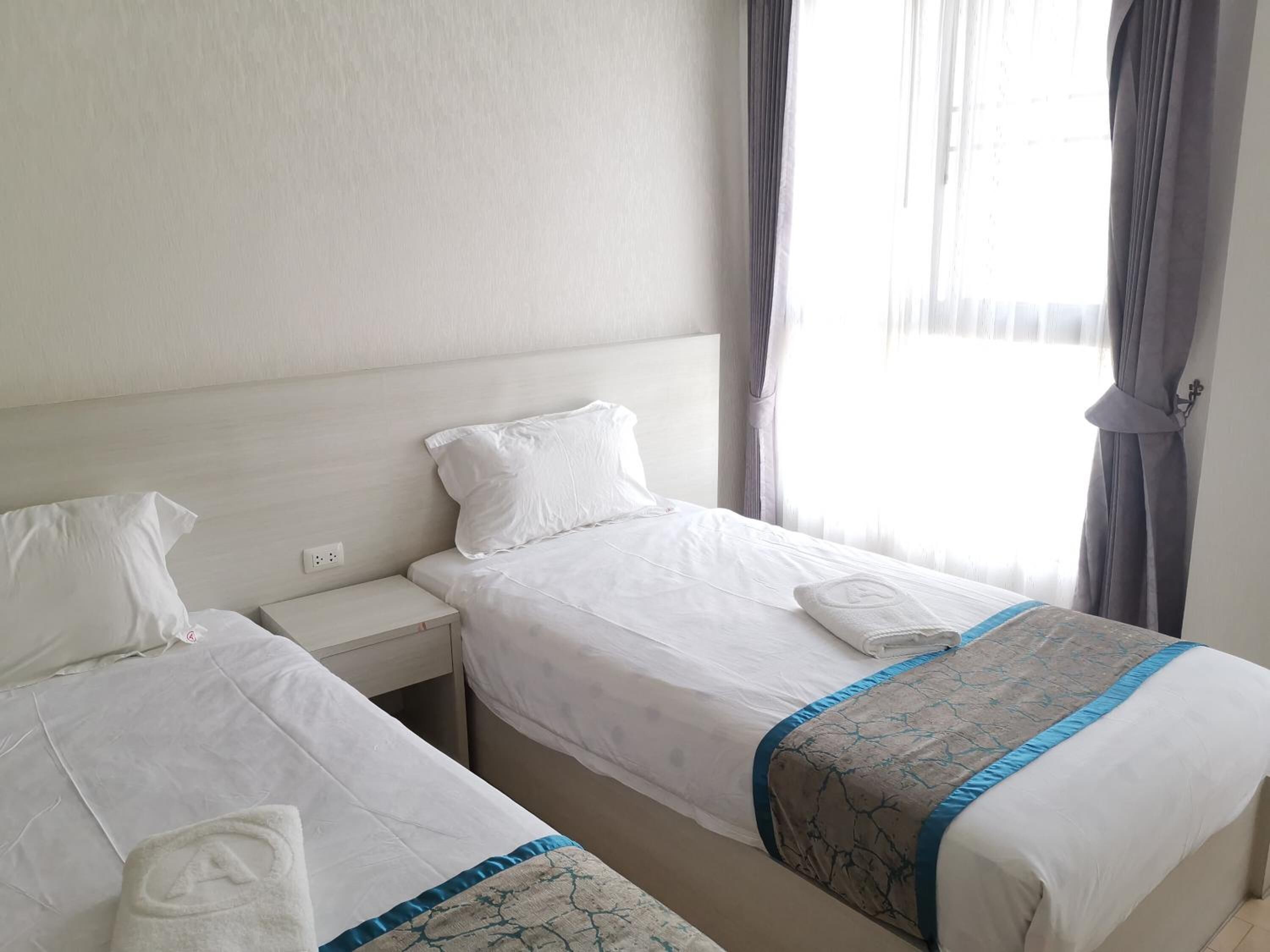 A hotel room with two single beds, a nightstand, and a window with curtains.