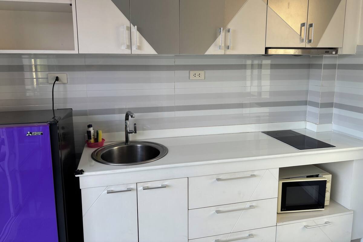 A modern kitchen with white cabinets, a stainless steel sink, a microwave, and a refrigerator.