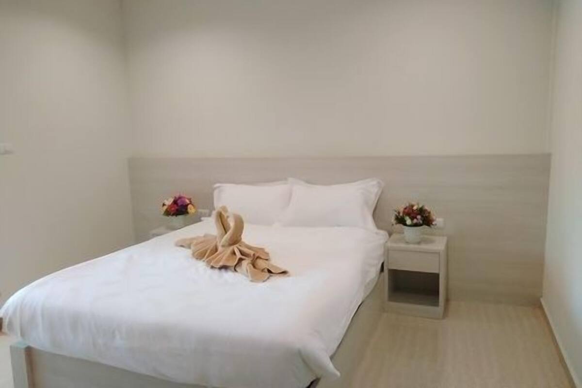A neatly made bed with a beige blanket and pillows, a bedside table with a vase of flowers, and a nightstand with a lamp.
