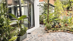 Une cour avec un sol en pierre, des plantes en pot et un bâtiment en briques doté de grandes fenêtres.
