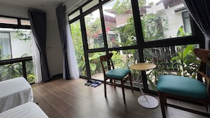 Une pièce avec de grandes fenêtres, un plancher en bois, une table ronde, deux chaises et un lit.