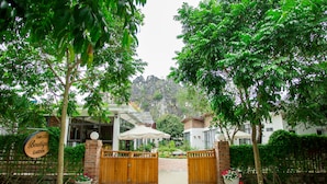 Une entrée fermée par un portail mène à une propriété sur laquelle est apposée une enseigne indiquant : « TAM COC, jardin-boutique ».