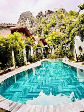 Une piscine dont le fond est décoré d’un motif en chevrons, entourée d’une végétation luxuriante et avec une chaîne de montagnes en toile de fond.