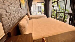 Une chambre d’hôtel avec un mur en briques, deux lits, une table en bois et de grandes fenêtres avec des rideaux.