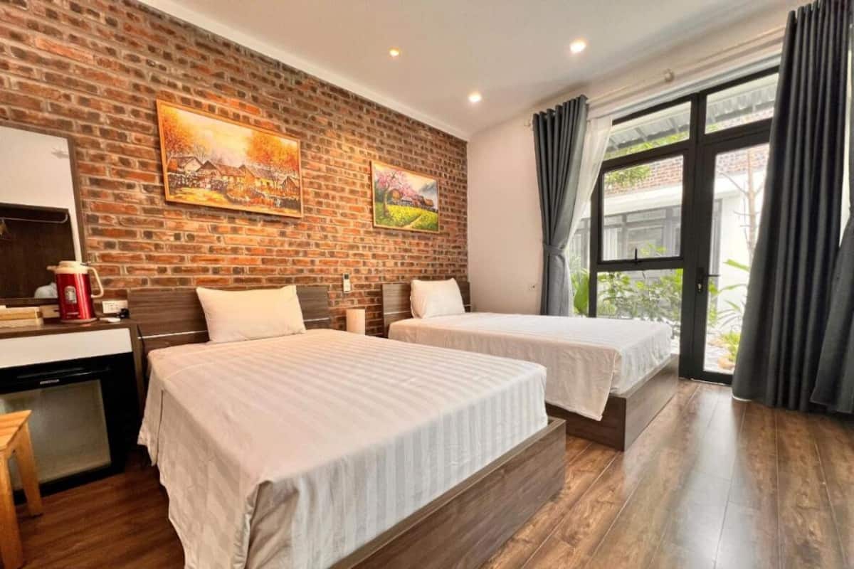 A hotel room with two beds, a brick wall, and a large window with curtains.