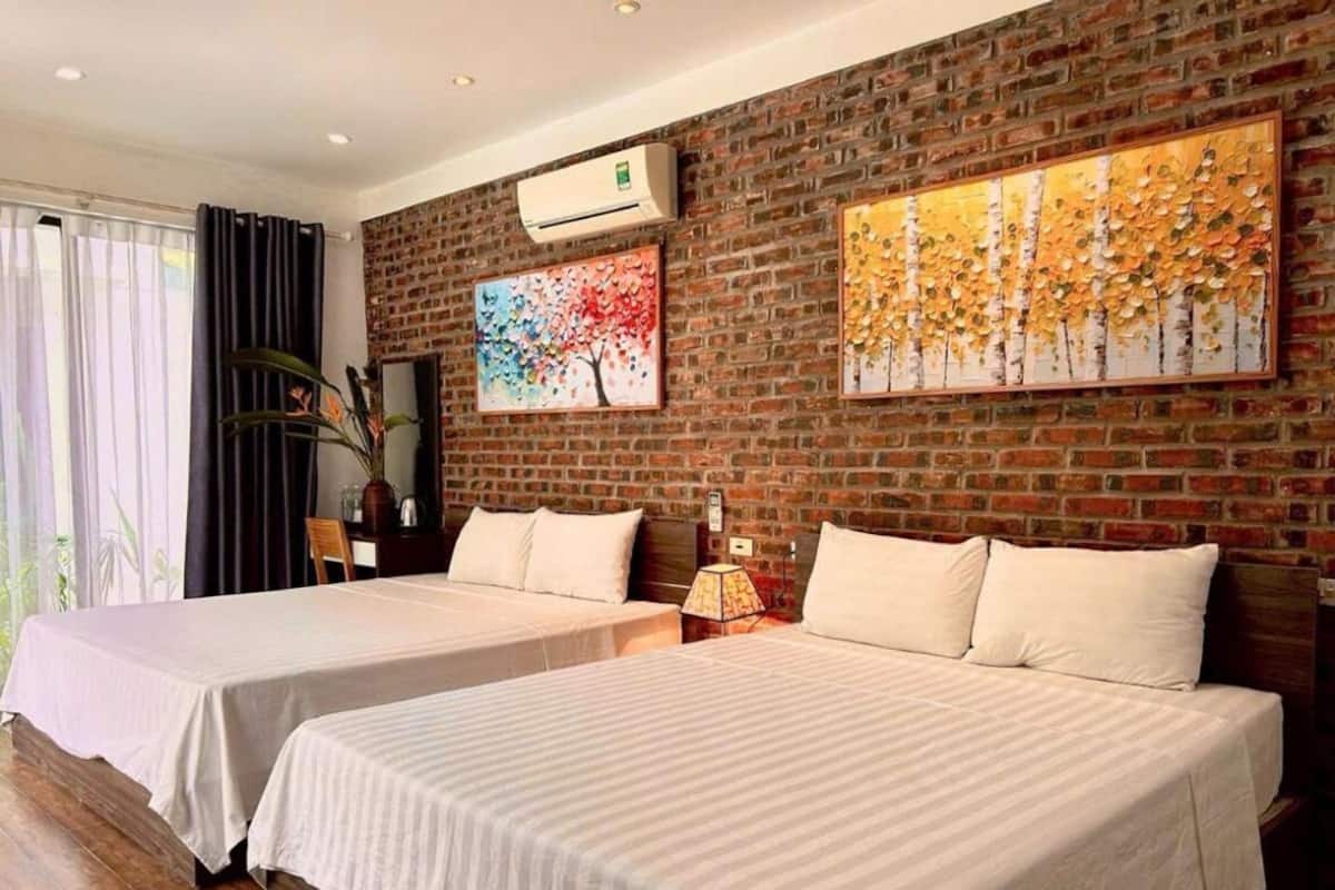 A hotel room with two beds, a brick wall, and two paintings.