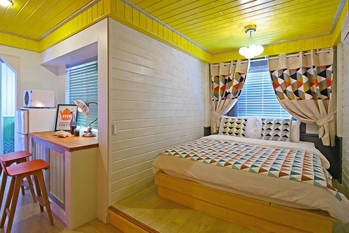 Um quarto com uma cama, uma escrivaninha com cadeira e uma janela com cortinas.