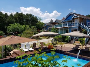 A swimming pool with lounge chairs and umbrellas, surrounded by a wooden deck and lush greenery.