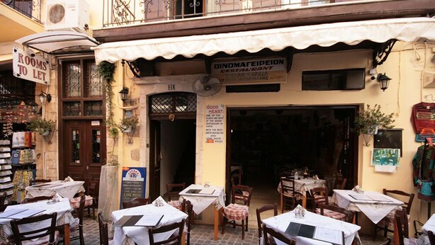 An outdoor dining area with tables and chairs, a sign for 'Rooms to Let', and a restaurant named 'Dinomareideion'. - Chania Rooms (Chania)