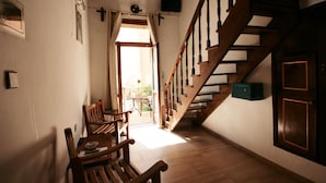 A room with a wooden staircase, a dining area with wooden chairs and a table, and a view of the outside through a door. - Chania Rooms (Chania)