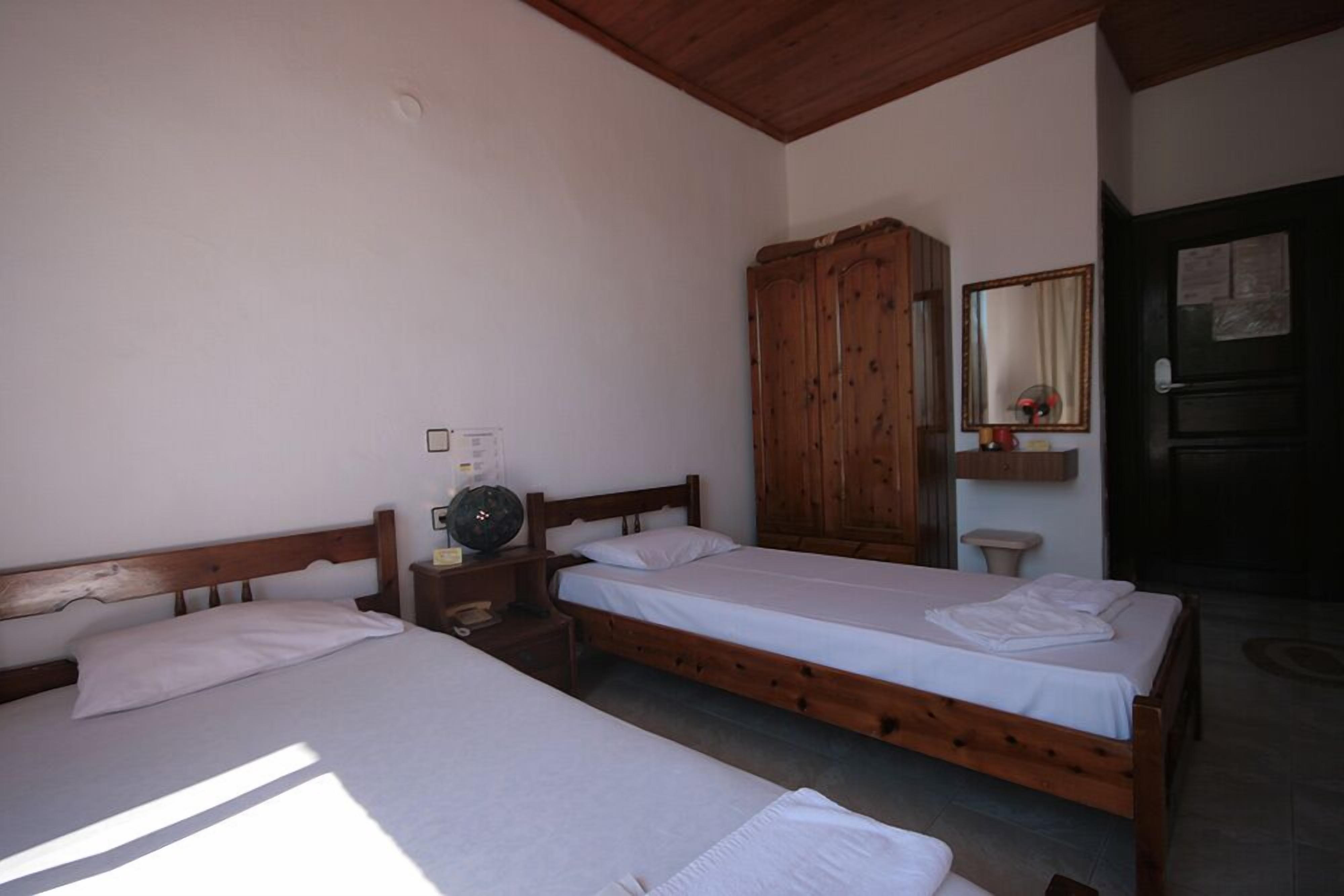A room with two wooden beds, a wooden wardrobe, a bedside table with a lamp, and a mirror on the wall.