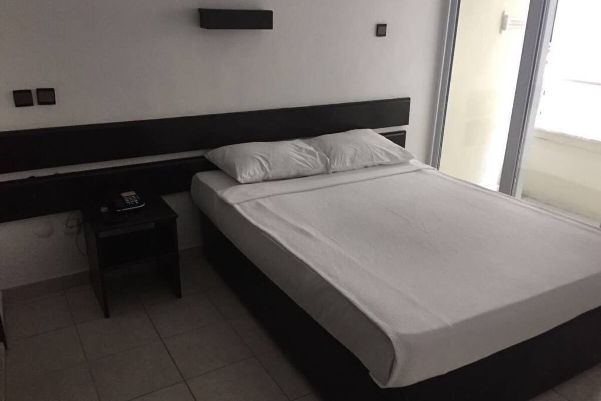 A modern hotel room with a large bed, a bedside table with a phone, and a window with a view.