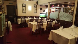 A restaurant interior with multiple tables and chairs, a bar area, and decorative wall art. - Kirkenes Hotel (South Varanger)