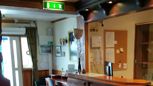 A restaurant with wooden flooring, a counter, and a seating area with tables and chairs. - Kirkenes Hotel (South Varanger)