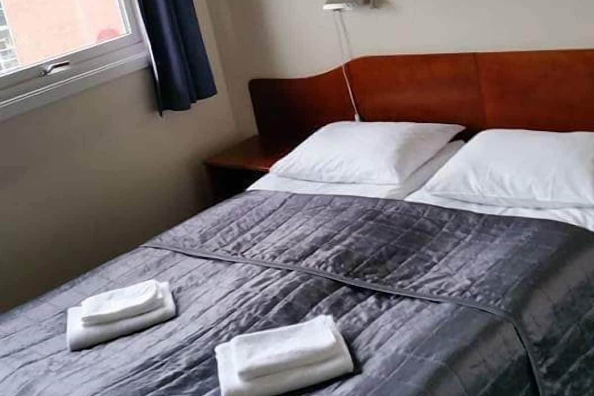 A hotel room with a bed, a headboard, a window with curtains, and a wall mural.