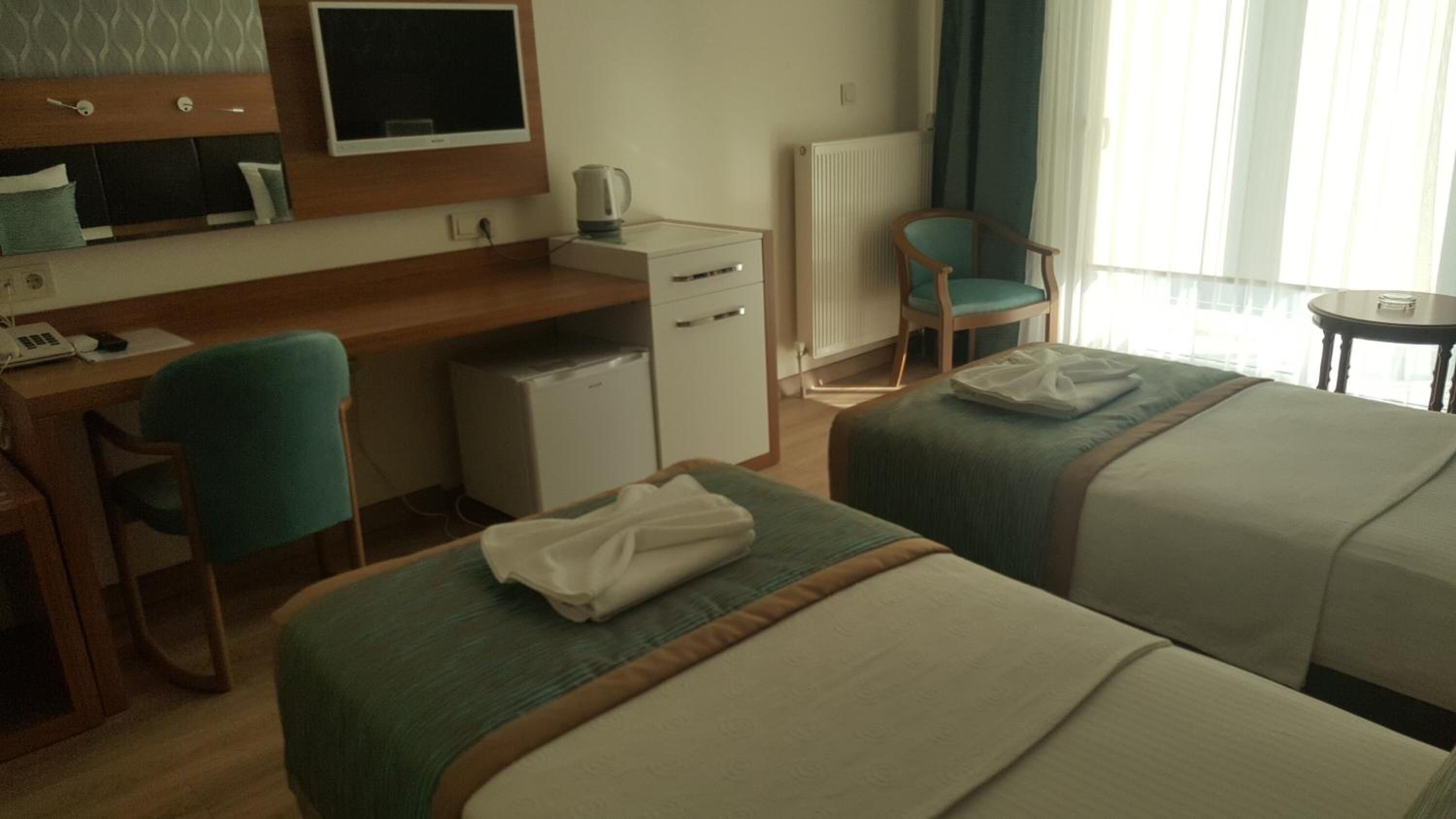 Une chambre d’hôtel avec deux lits, un bureau, une chaise, un radiateur et un téléviseur.