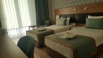 A hotel room with two beds, a chair, a small table, and a window with curtains.