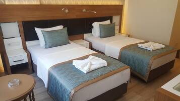 Habitación de hotel con dos camas, cada una con cabecero de madera, ropa de cama blanca y almohadones turquesa. Hay una pequeña mesa redonda con una toalla, y una mesita de noche blanca con una lámpara.