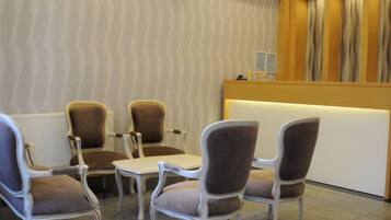 A reception area with a reception desk, two brown upholstered chairs, and a white table.