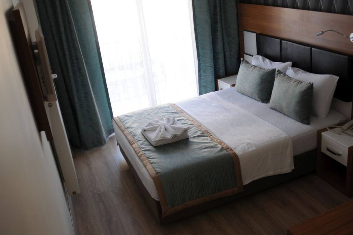 Une chambre d’hôtel avec un lit, une table de chevet, une tête de lit en bois et une fenêtre avec des rideaux.