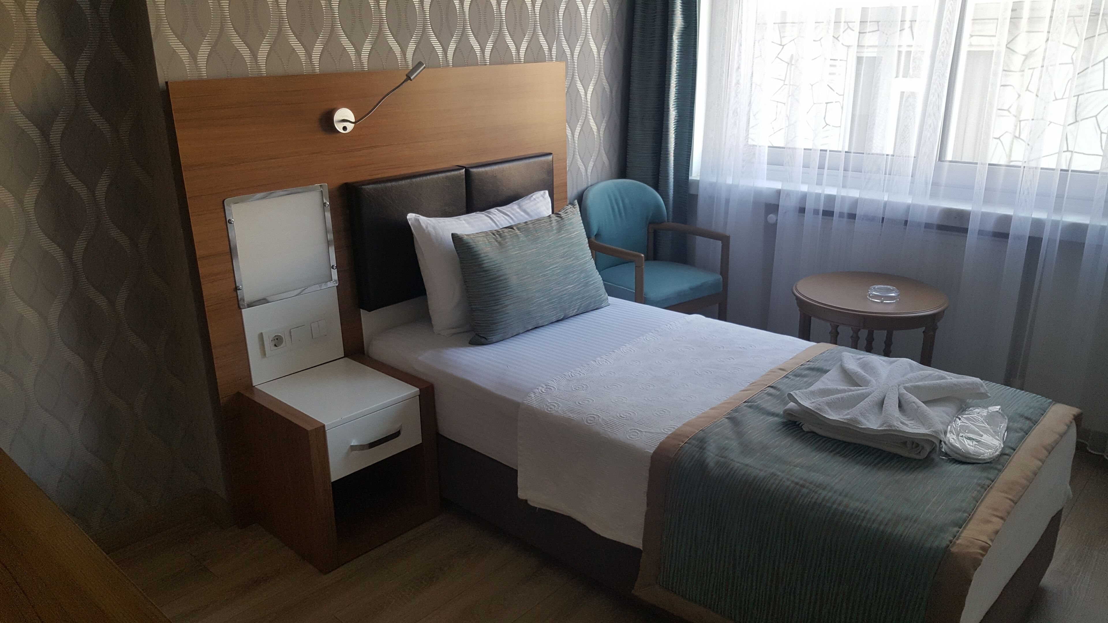 A hotel room with a bed, bedside table, chair, and a small table.