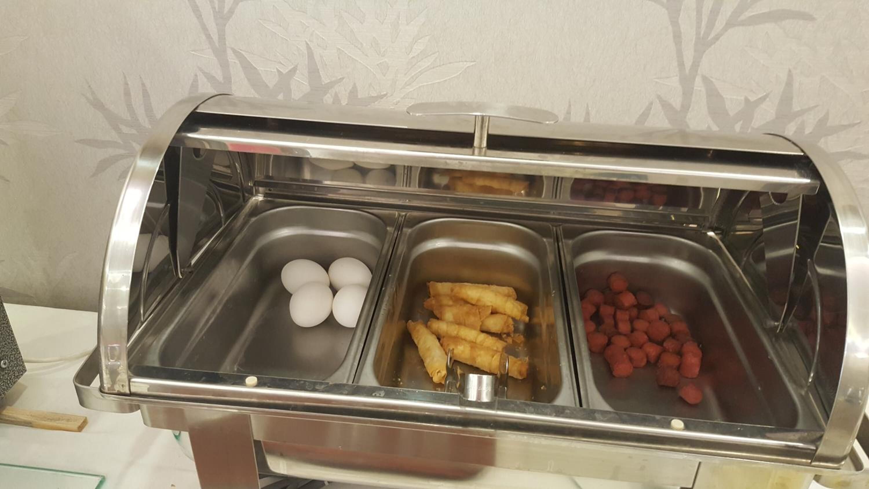 A buffet with three food stations: eggs, fried items, and sausages.