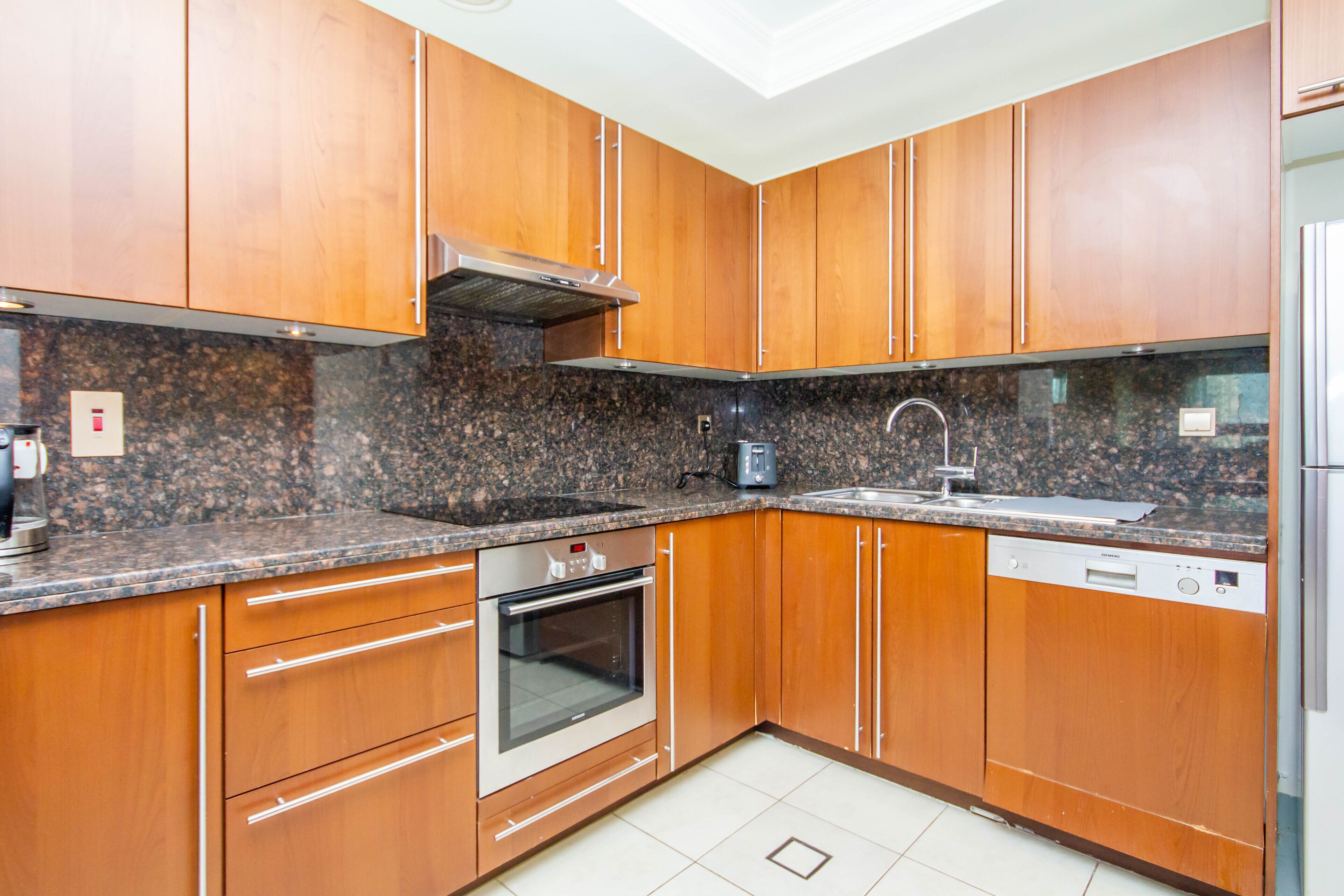 A kitchen with wooden cabinets, granite countertops, a stainless steel range hood, a dishwasher, and a built-in oven.