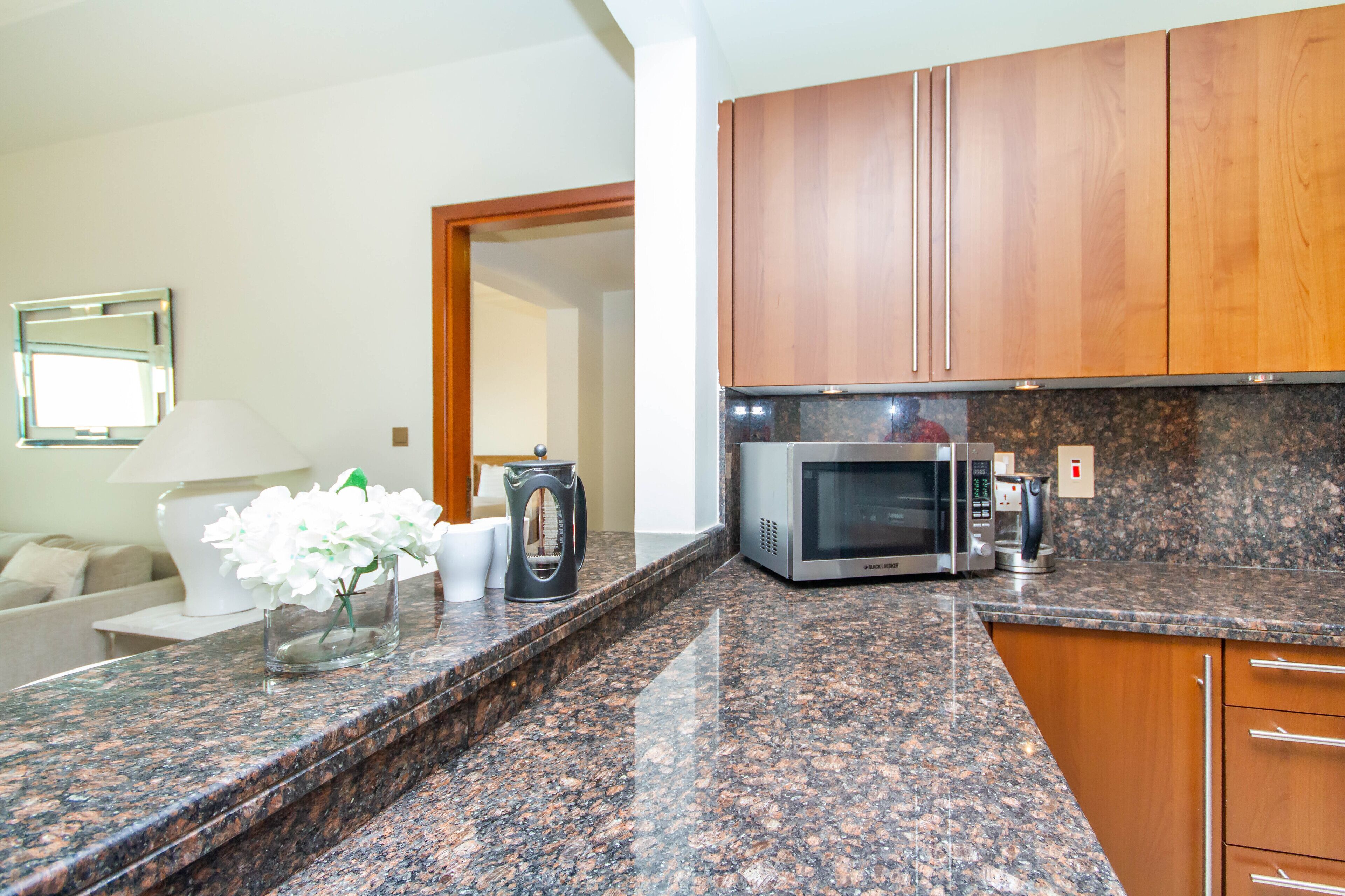 A kitchen with granite countertops, wooden cabinets, a microwave, and a coffee maker.