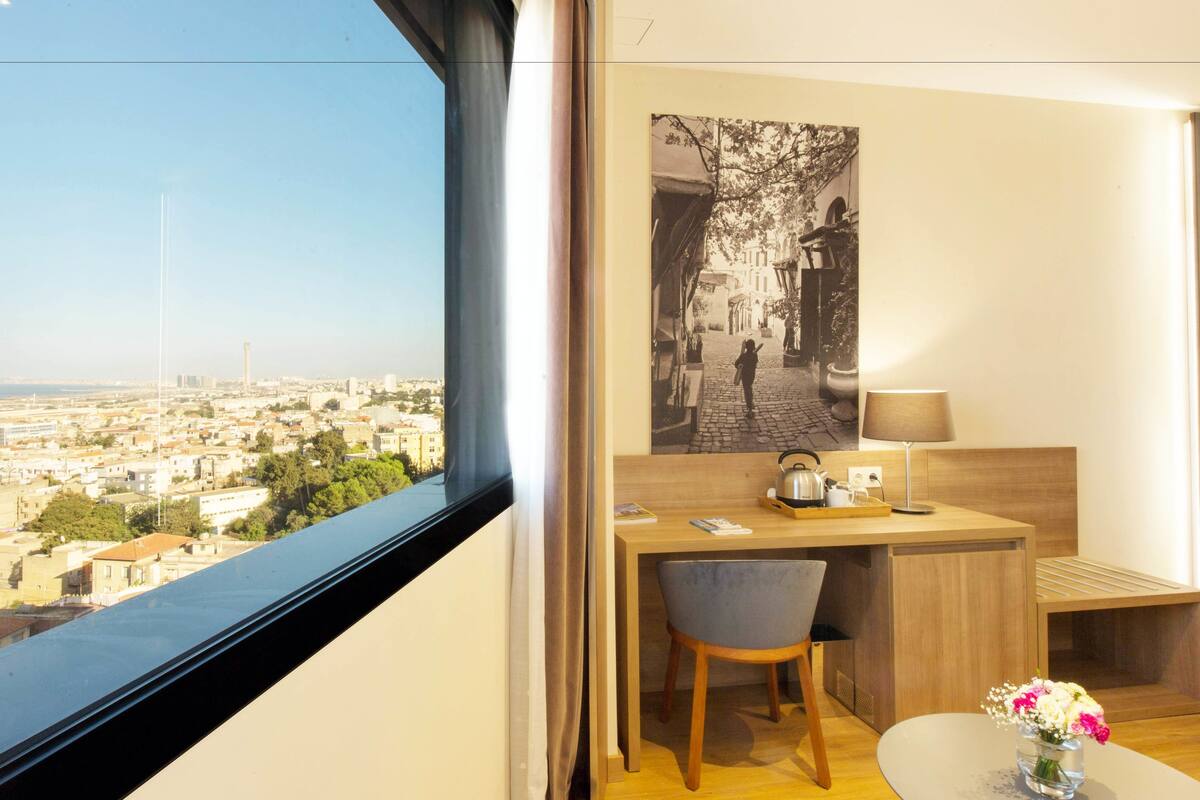 A hotel room with a desk, chair, and a view of the cityscape.