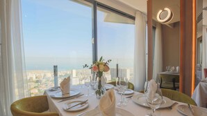 A dining table set for four with a view of a cityscape through large windows. - Lamaraz Arts Hotel (Algiers)