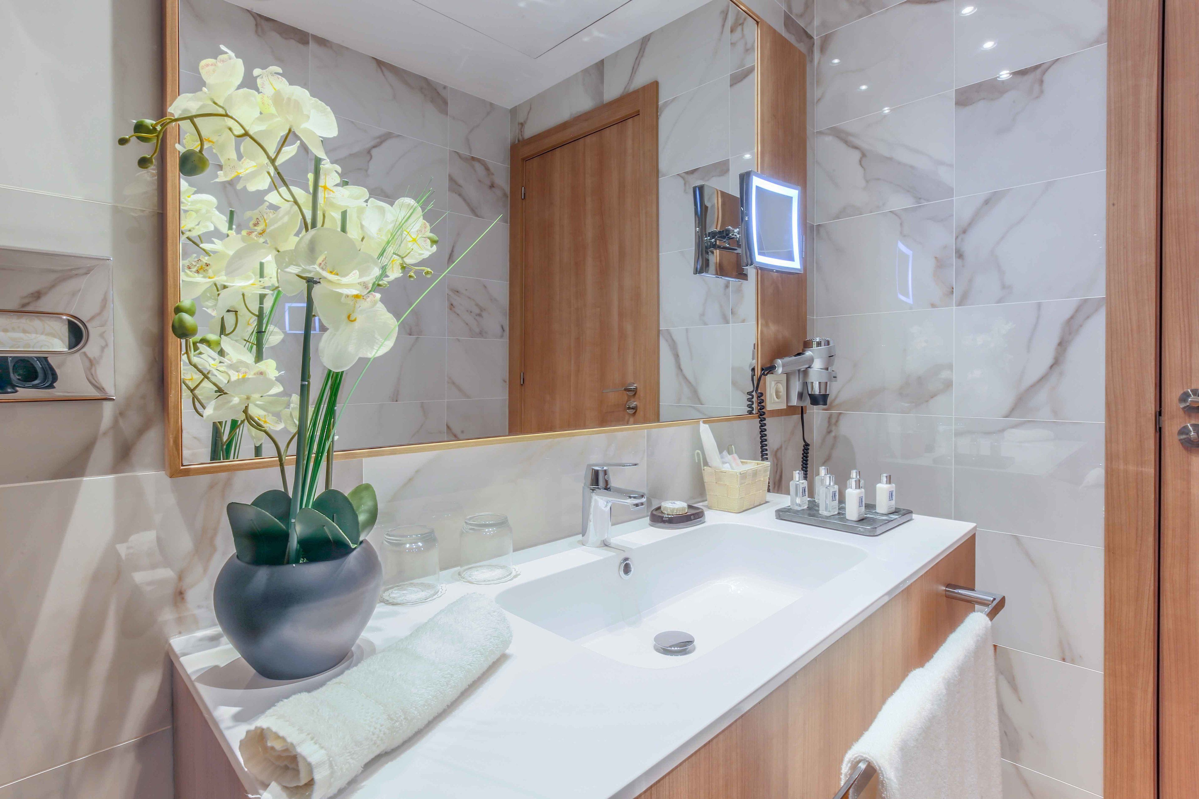 Ein modernes Badezimmer mit einem мраморным Waschbecken, einem großen Spiegel und einer Vase mit weißen Orchideen.