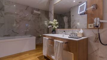 A modern bathroom with a marble wall, a wooden vanity, a large mirror, a built-in shower, and a towel rack.