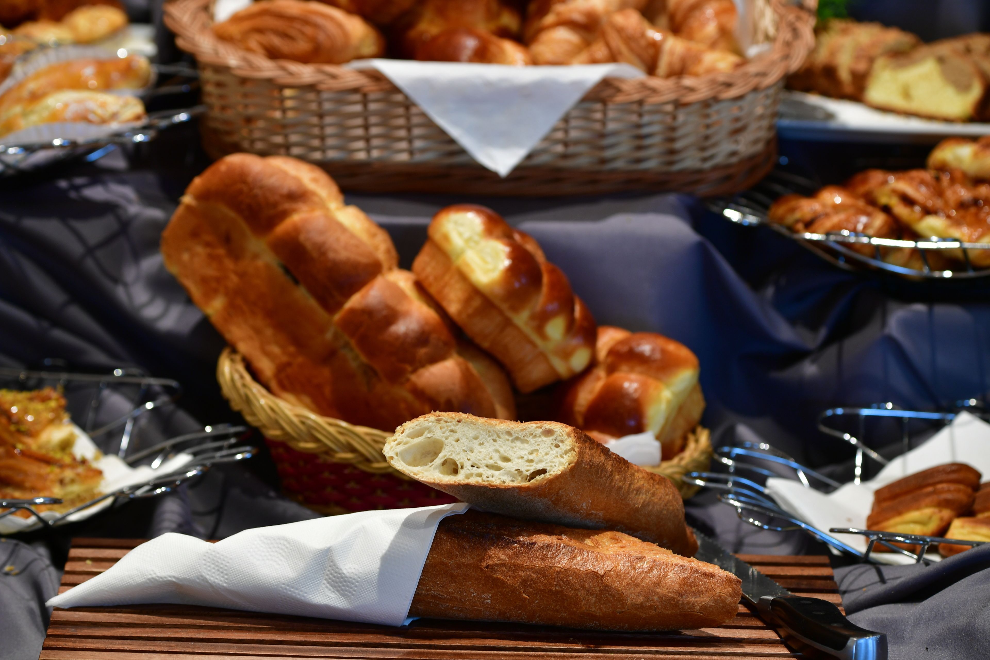 Variedad de panes y pasteles sobre una mesa, incluyendo una cesta de croissants y una hogaza.