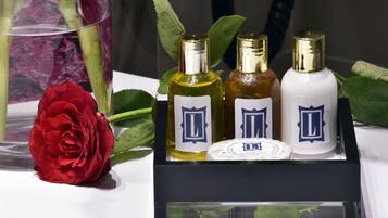 Exhibición de cuatro botellas de perfume con un recipiente jabonero redondo central, una rosa roja y hojas verdes sobre una superficie blanca.