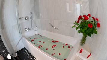 Un baño moderno con ducha de vidrio, bañera con pétalos de rosa y un florero con rosas rojas.