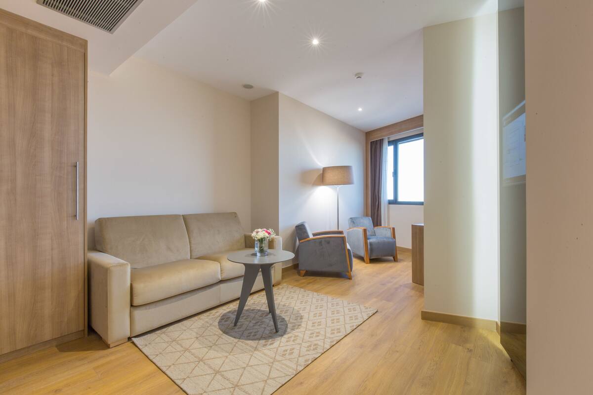 A modern living room with a sofa, a small table with a vase, and a lamp.