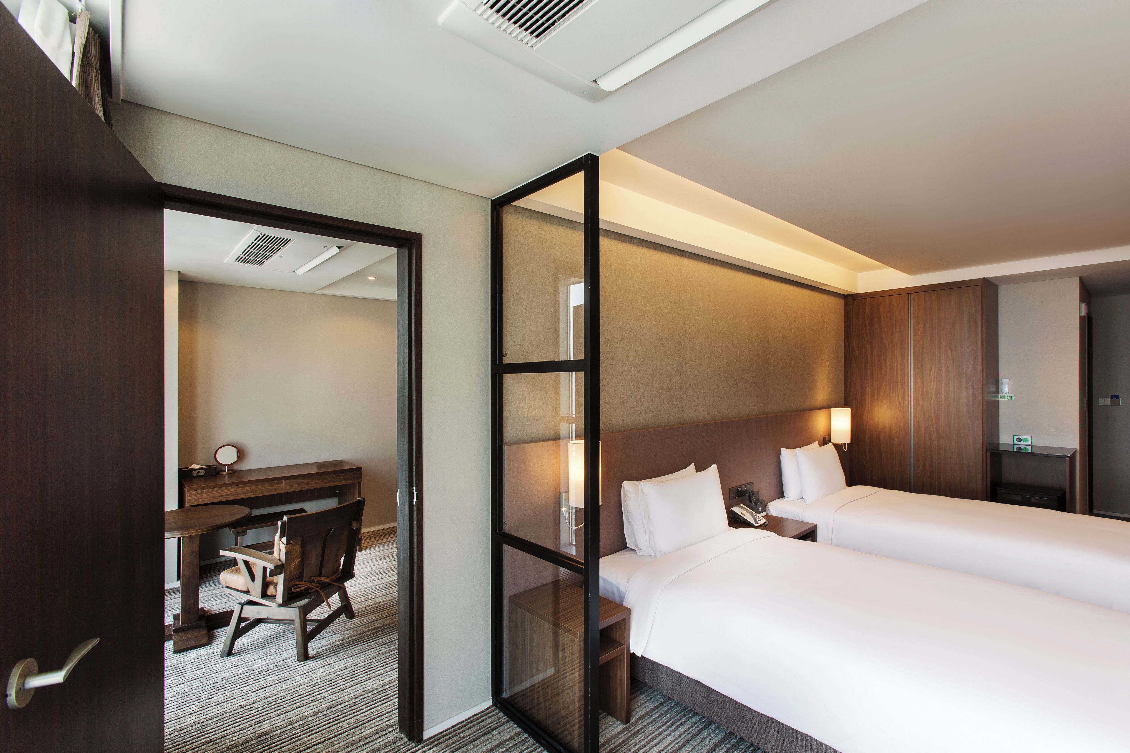 A hotel room with a desk, two beds, a mirror, and a nightstand.