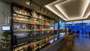 En moderne bar med en høj bardisk, hylder med spiritusflasker og udsigt over byen gennem store vinduer.