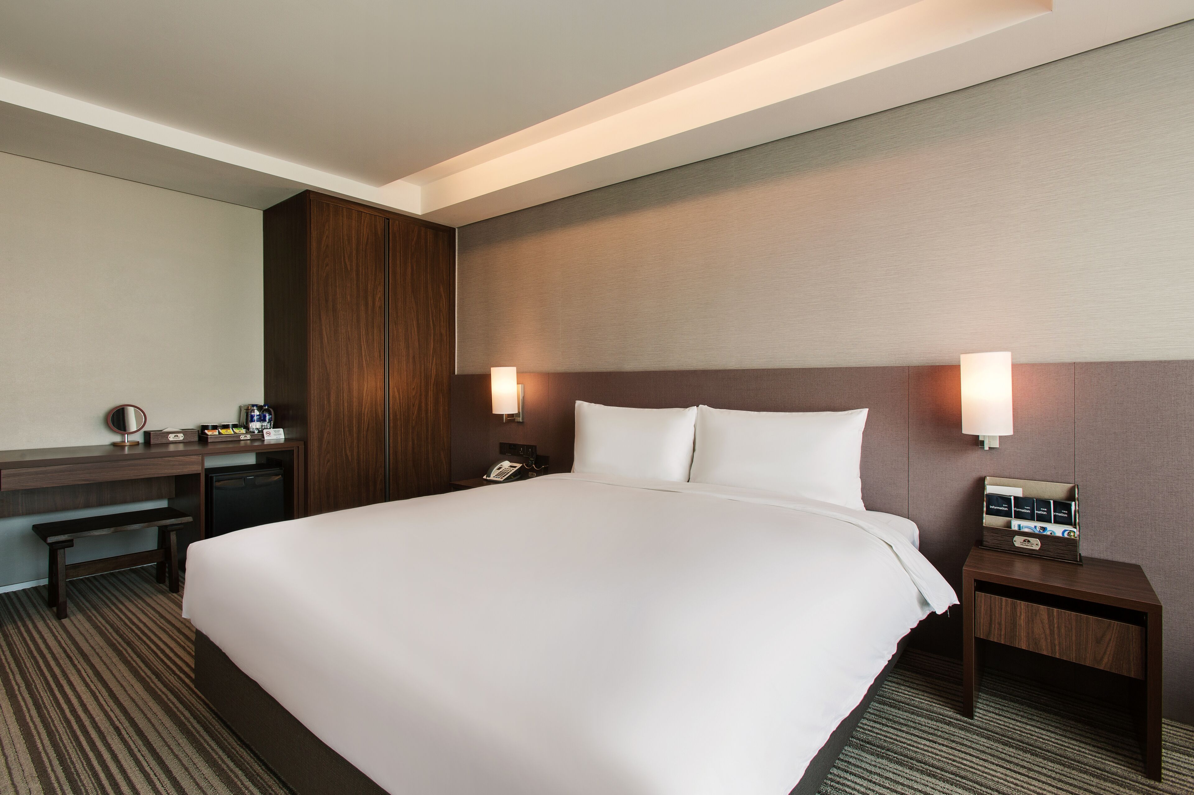 Une chambre d’hôtel avec un grand lit, un bureau avec un miroir, un téléphone et une table de chevet avec une lampe.