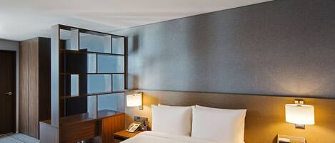 Habitación de hotel con una cama grande, un escritorio con teléfono, dos lámparas de noche y un televisor de pared.