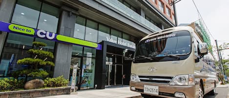 A Value Hotel Busan with a modern facade, a large entrance, and a parked bus in front.