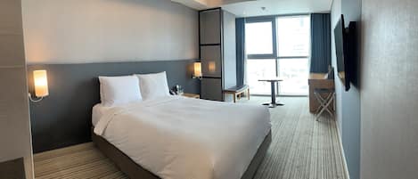 Una habitación de hotel con una cama grande, mesitas de noche, un escritorio, una silla y un televisor fijado a la pared.