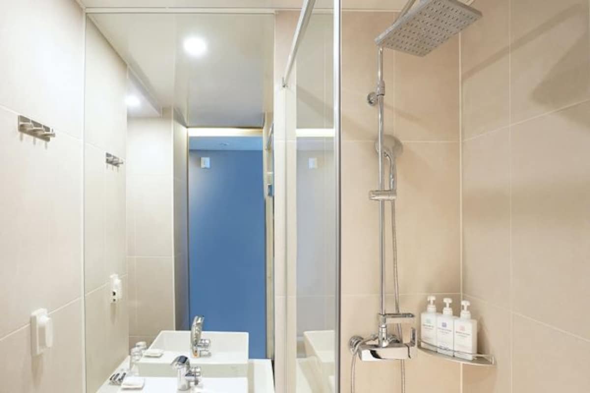A modern bathroom with a glass-enclosed shower, a sink with a mirror, and a shelf with toiletries.