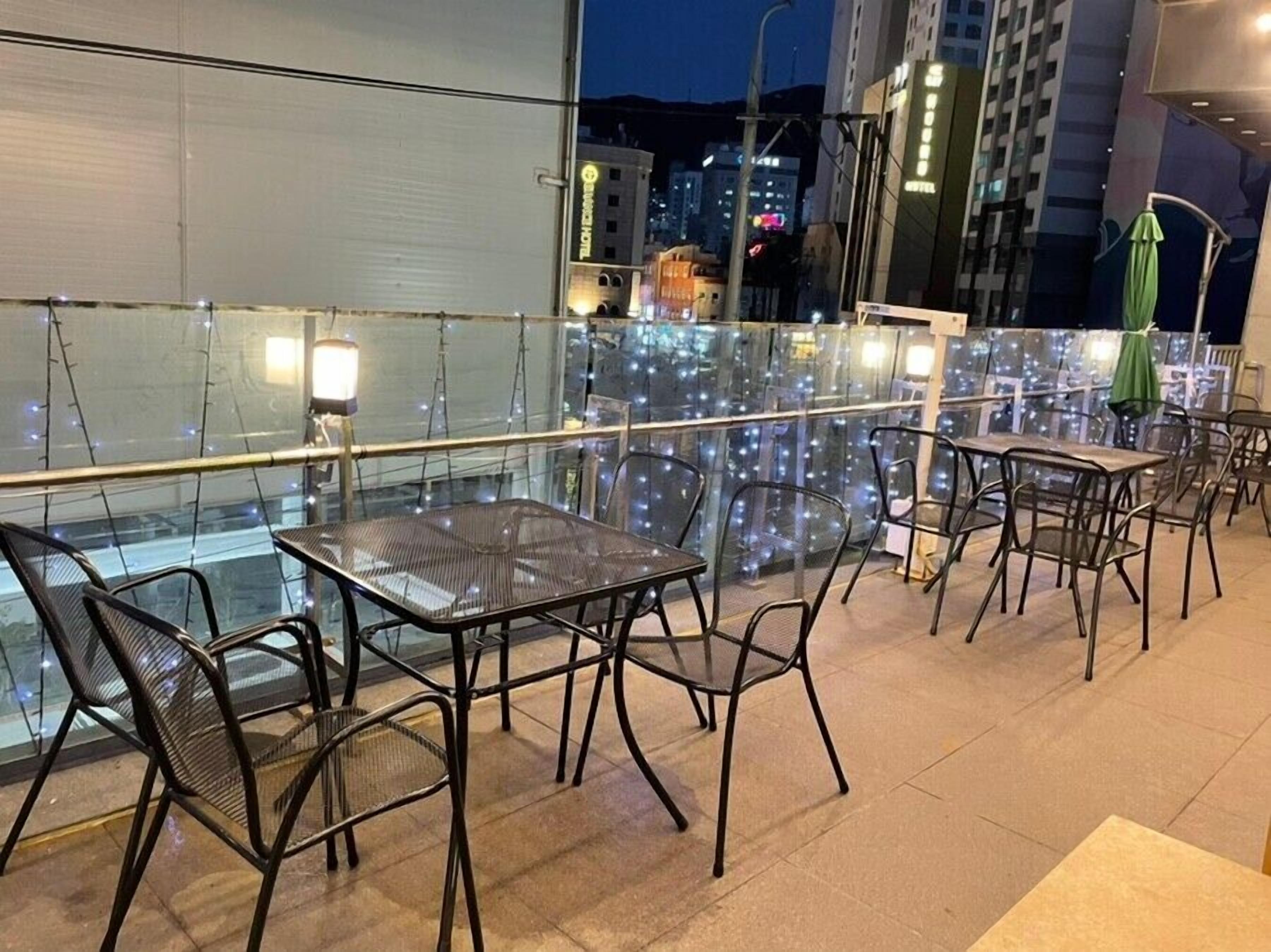 An outdoor terrace with glass tables and chairs, a railing, and a view of the cityscape at night.
