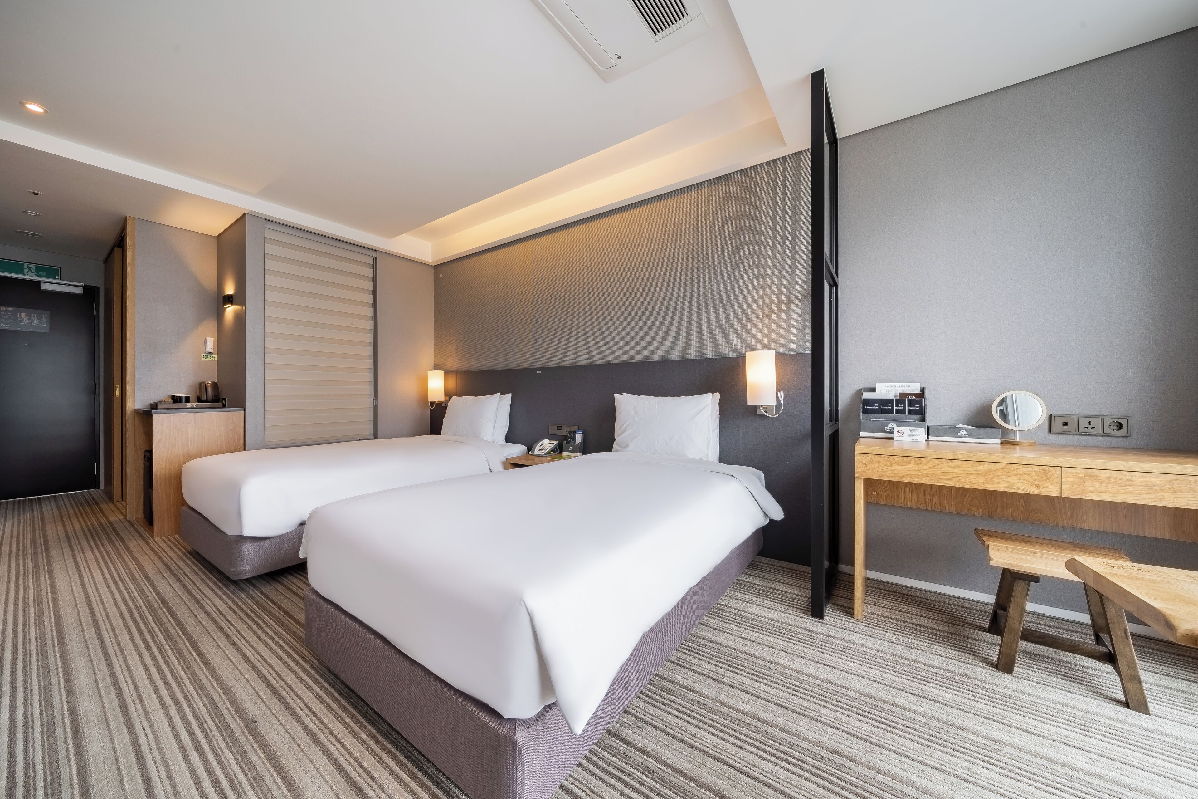A hotel room with two beds, a desk, a chair, a telephone, and a wall-mounted light.