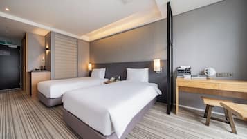 A hotel room with two beds, a desk, a chair, a telephone, and a wall-mounted light.