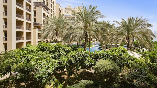 A hotel with multiple floors, balconies, and a pool area surrounded by palm trees and greenery. - Bespoke Residences - North Residence (Dubai)