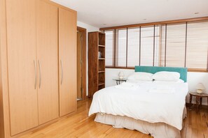 A bedroom with a bed, wooden wardrobe, and a window with blinds.